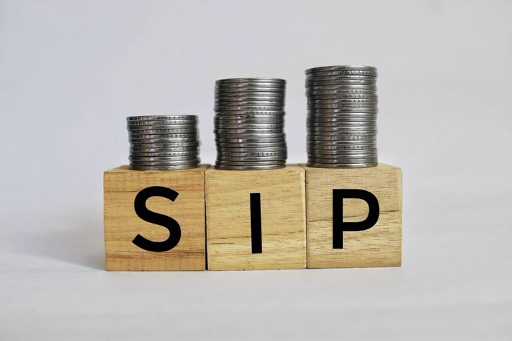 Stacks of coins placed on wooden blocks with letters SIP, symbolizing growth through systematic investment plans.